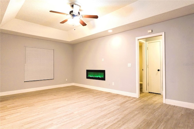 unfurnished room with light wood-style floors, baseboards, a tray ceiling, and a glass covered fireplace