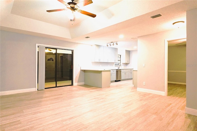 interior space featuring baseboards, visible vents, a ceiling fan, a tray ceiling, and light wood-style floors
