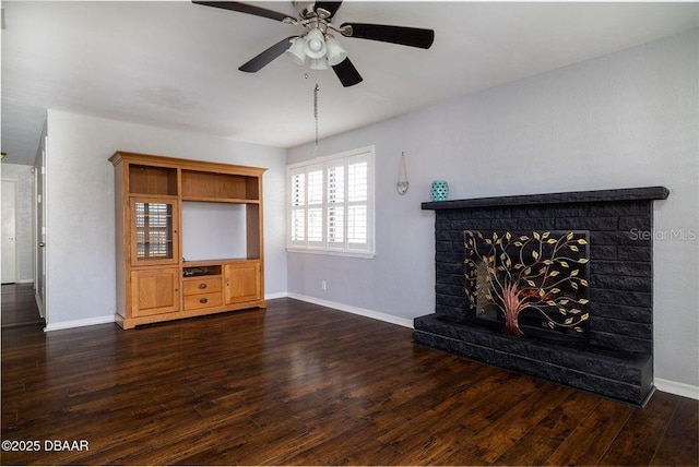 unfurnished living room featuring dark wood-type flooring, a brick fireplace, baseboards, and a ceiling fan