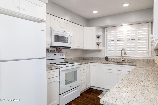 kitchen with white appliances, white cabinets, light stone counters, dark wood-type flooring, and a sink