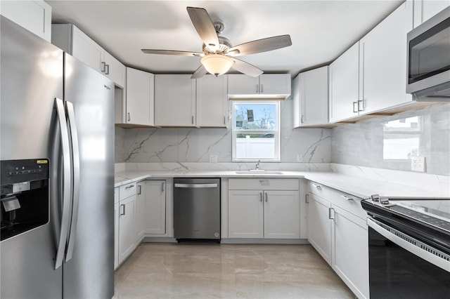 kitchen with light stone counters, a sink, a ceiling fan, appliances with stainless steel finishes, and tasteful backsplash