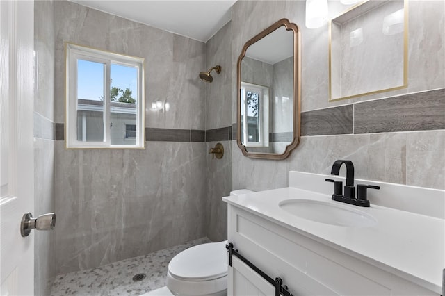 bathroom with toilet, vanity, a tile shower, and tile walls