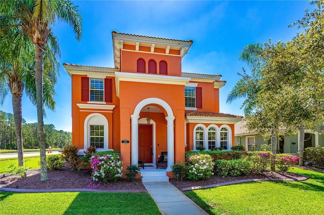 mediterranean / spanish house featuring a front lawn, a tiled roof, and stucco siding