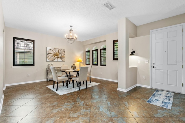 dining room with a textured ceiling, visible vents, baseboards, and a chandelier