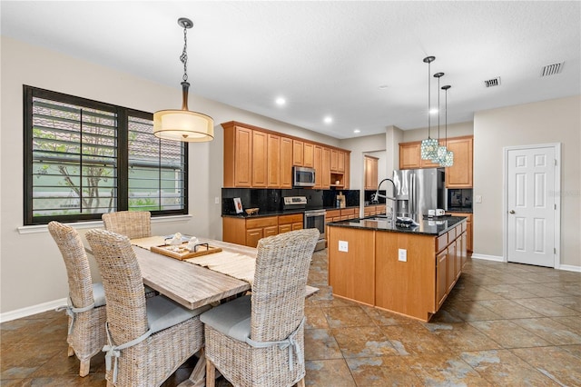 kitchen with visible vents, a center island with sink, backsplash, appliances with stainless steel finishes, and baseboards