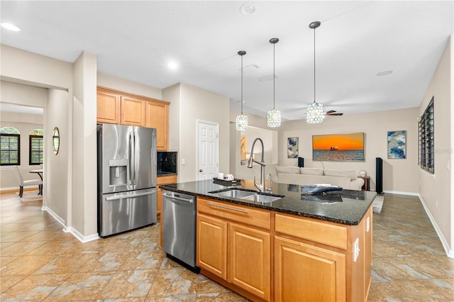 kitchen featuring dark stone countertops, an island with sink, a sink, appliances with stainless steel finishes, and open floor plan