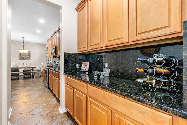 kitchen featuring backsplash, dark stone counters, light tile patterned floors, appliances with stainless steel finishes, and hanging light fixtures