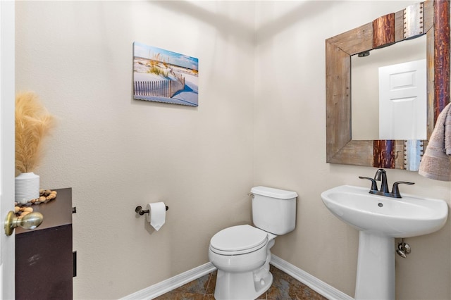 half bathroom featuring toilet, baseboards, and a sink