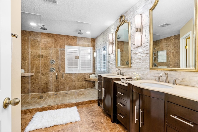 full bath with visible vents, two vanities, a stall shower, a sink, and a textured ceiling