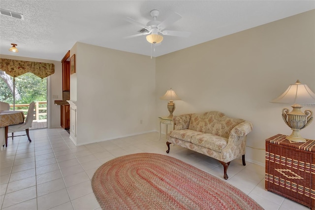 living area featuring a textured ceiling, light tile patterned flooring, visible vents, baseboards, and a ceiling fan