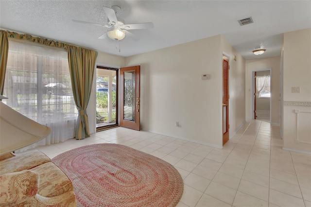 foyer with a textured ceiling, ceiling fan, light tile patterned flooring, visible vents, and baseboards