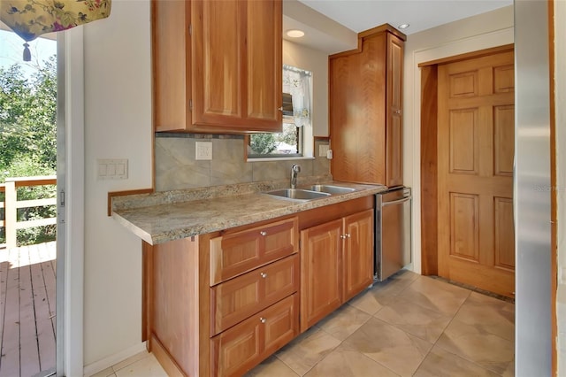 kitchen with light tile patterned floors, a sink, decorative backsplash, dishwasher, and brown cabinetry