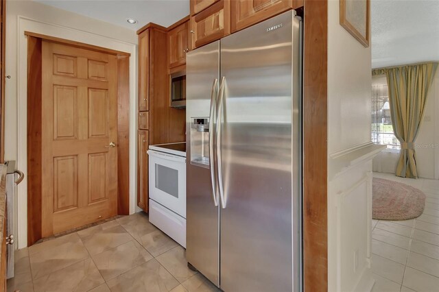 kitchen featuring light tile patterned floors, appliances with stainless steel finishes, and brown cabinetry