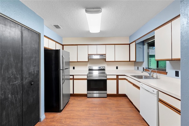 kitchen featuring stainless steel appliances, light countertops, a sink, wood finished floors, and under cabinet range hood