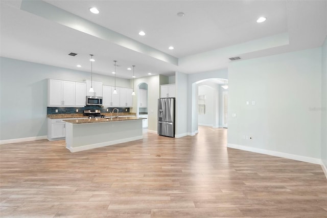 kitchen featuring arched walkways, stainless steel appliances, visible vents, open floor plan, and light wood finished floors