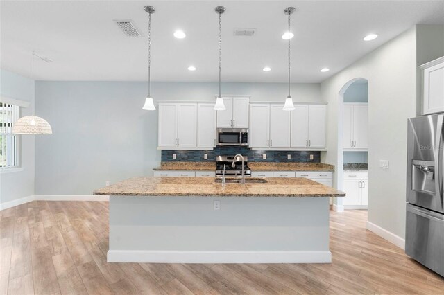 kitchen with arched walkways, backsplash, appliances with stainless steel finishes, a kitchen island with sink, and a sink