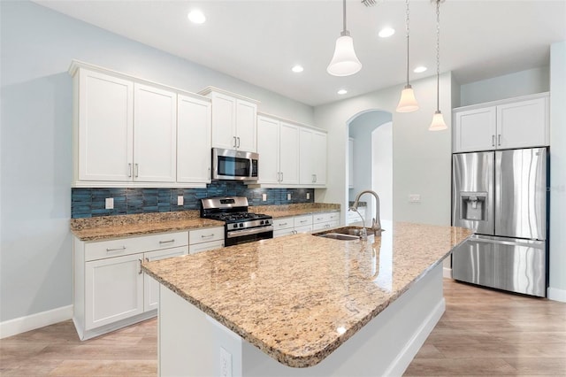 kitchen featuring arched walkways, stainless steel appliances, a sink, light wood-type flooring, and backsplash