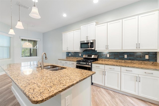 kitchen featuring appliances with stainless steel finishes, a sink, light wood-style flooring, and tasteful backsplash