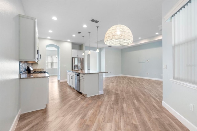 kitchen with arched walkways, a center island with sink, recessed lighting, appliances with stainless steel finishes, and light wood-style floors