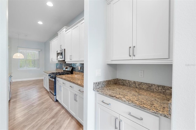 kitchen with light stone counters, light wood-style flooring, white cabinets, appliances with stainless steel finishes, and backsplash