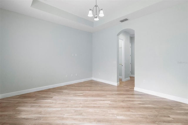 spare room featuring arched walkways, visible vents, a raised ceiling, and light wood-style flooring