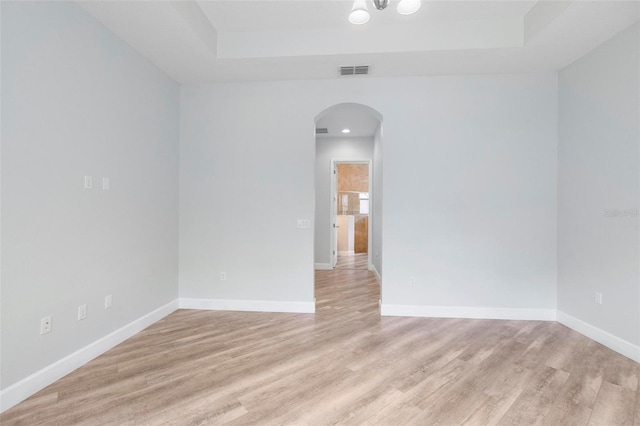 empty room with arched walkways, light wood-style flooring, and baseboards