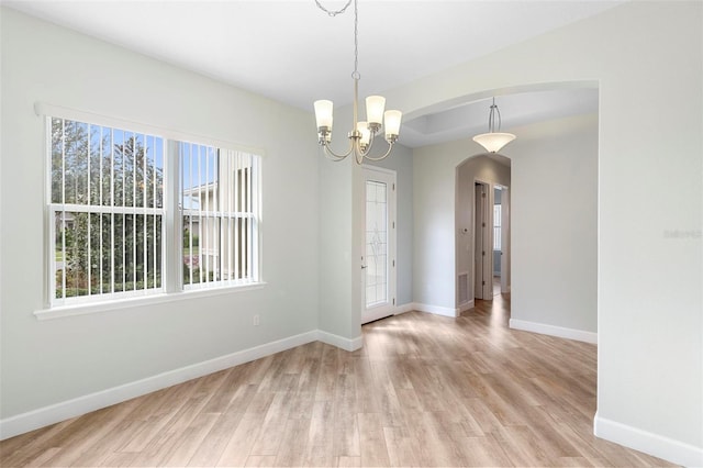 spare room with arched walkways, visible vents, light wood-style floors, a chandelier, and baseboards