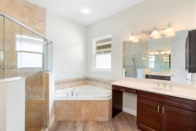 bathroom with a bath, two vanities, wood finished floors, a shower stall, and a sink