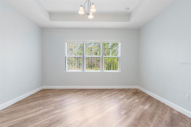 empty room featuring light wood finished floors, a tray ceiling, and baseboards