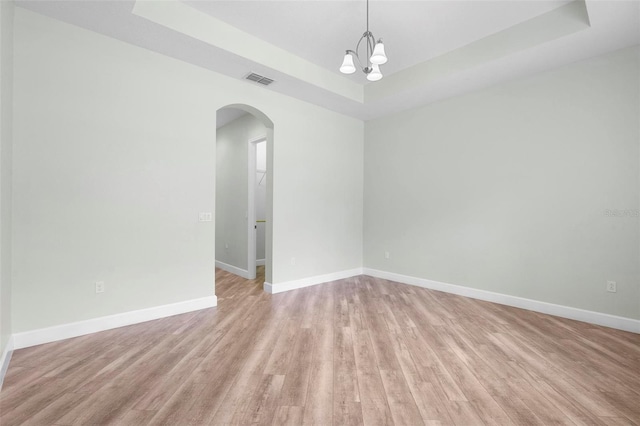 spare room with light wood-type flooring, baseboards, arched walkways, and a raised ceiling