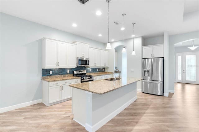 kitchen with tasteful backsplash, arched walkways, appliances with stainless steel finishes, a kitchen island with sink, and a sink