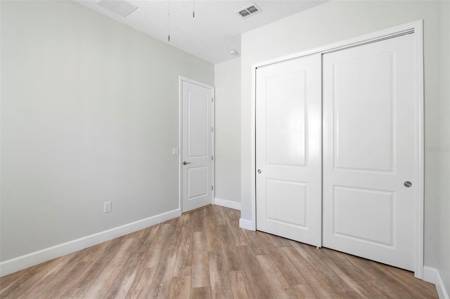 unfurnished bedroom with light wood-style flooring, visible vents, baseboards, and a closet