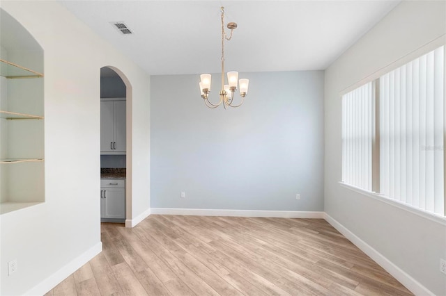 empty room featuring arched walkways, visible vents, an inviting chandelier, light wood-style floors, and baseboards