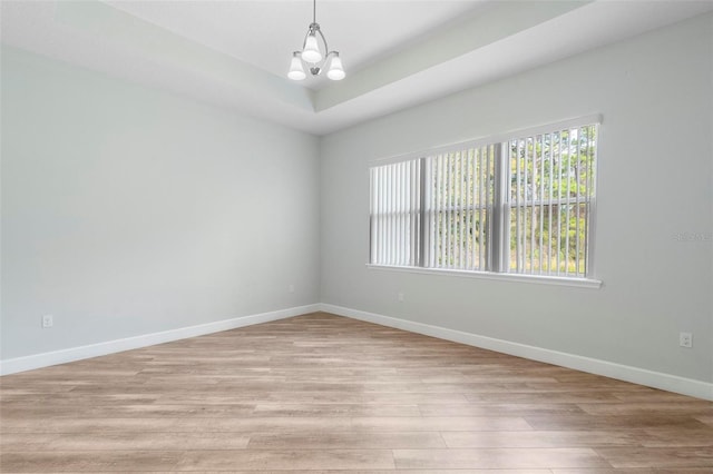 spare room with light wood-type flooring, baseboards, a raised ceiling, and a notable chandelier