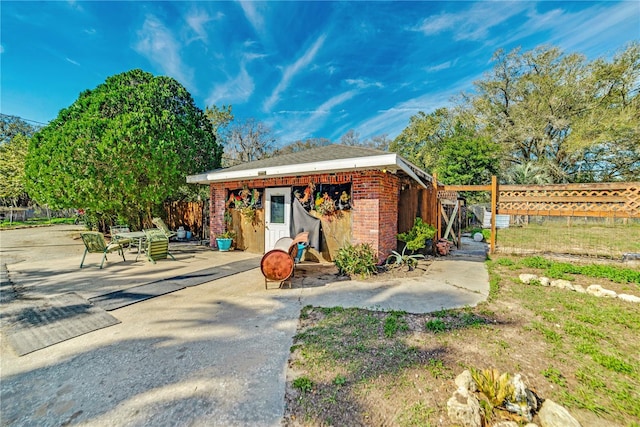 view of front facade featuring brick siding, fence, a patio, and an outdoor structure