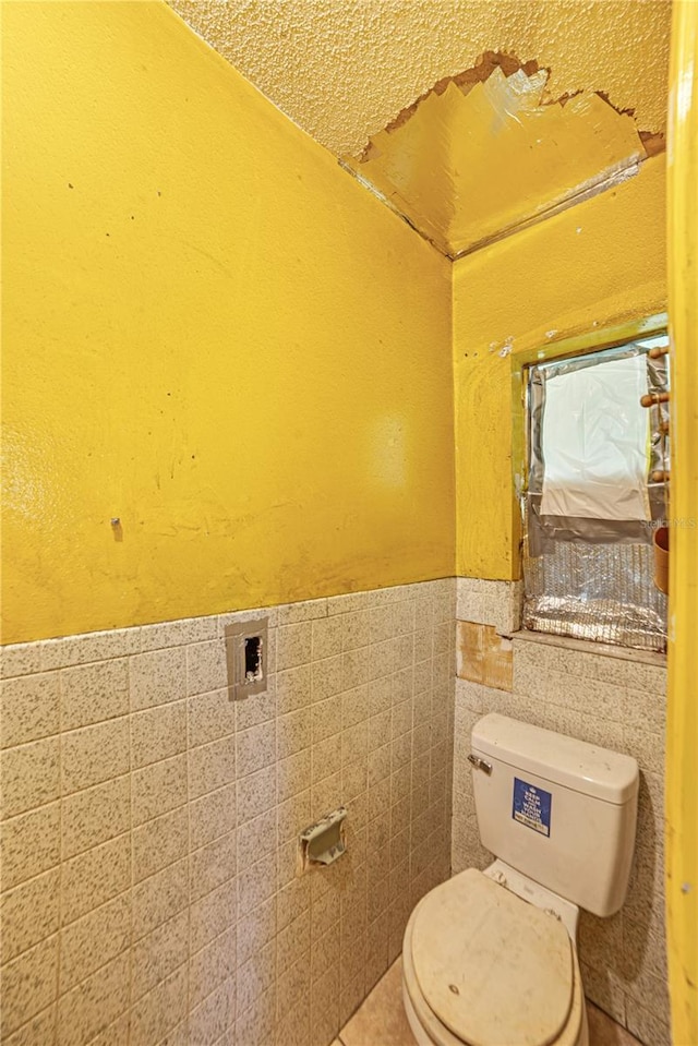 bathroom featuring toilet, tile walls, and wainscoting