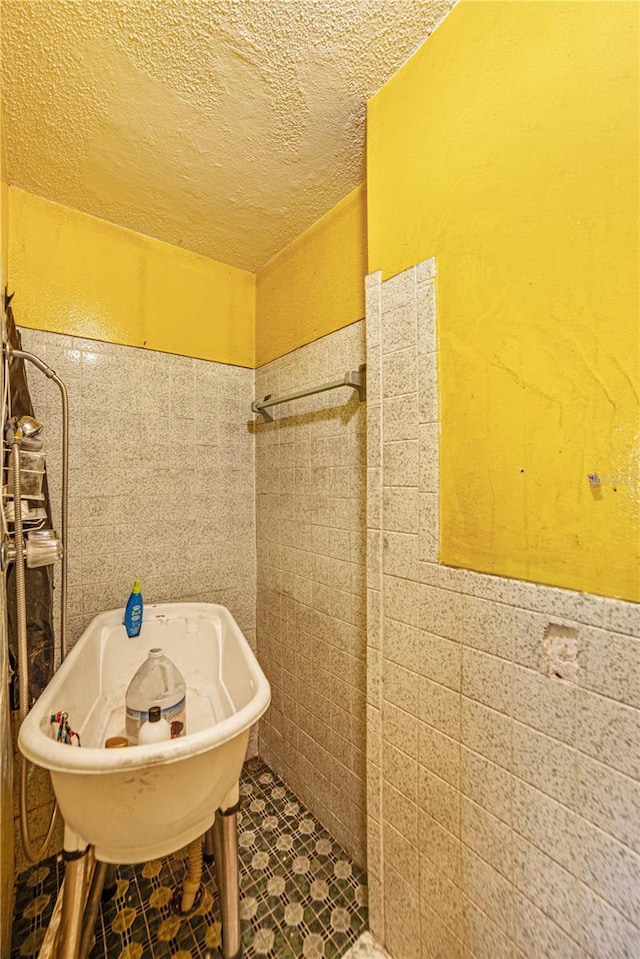 full bath with tile walls, wainscoting, a freestanding bath, and a textured ceiling