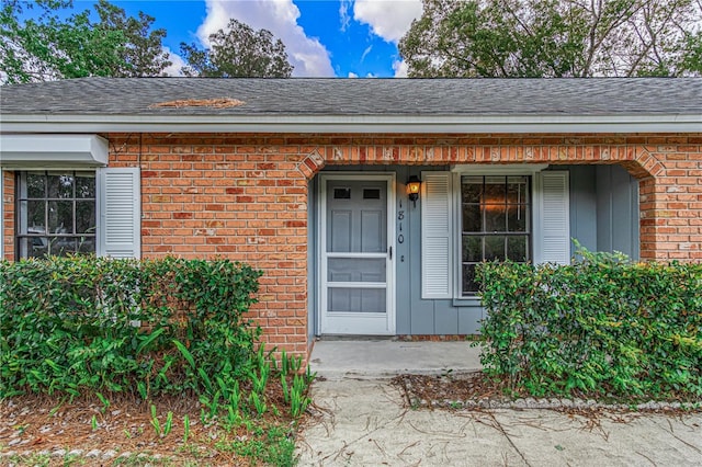 entrance to property with brick siding, roof with shingles, and board and batten siding