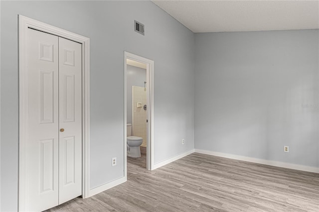 unfurnished bedroom with a closet, visible vents, connected bathroom, wood finished floors, and baseboards