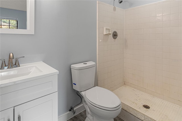 bathroom featuring toilet, wood finished floors, vanity, baseboards, and a tile shower