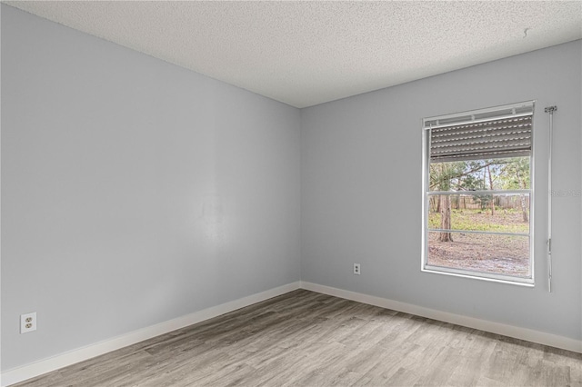 unfurnished room with a textured ceiling, wood finished floors, and baseboards