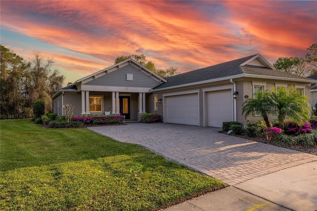 view of front facade featuring an attached garage, covered porch, decorative driveway, a yard, and stucco siding