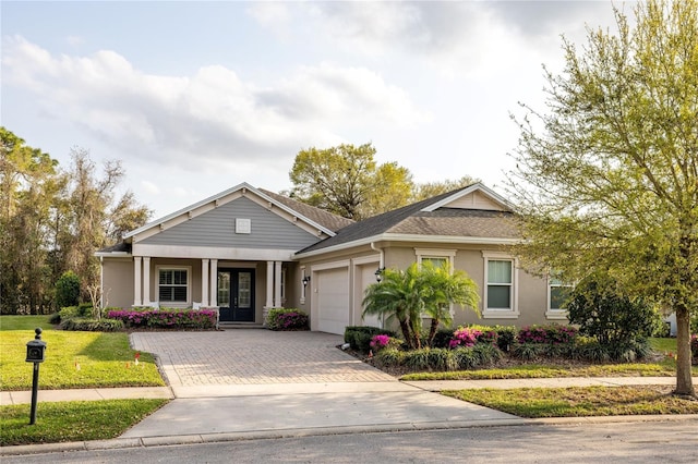 view of front of home featuring an attached garage, french doors, decorative driveway, stucco siding, and a front lawn