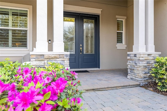 doorway to property featuring covered porch, stone siding, french doors, and stucco siding