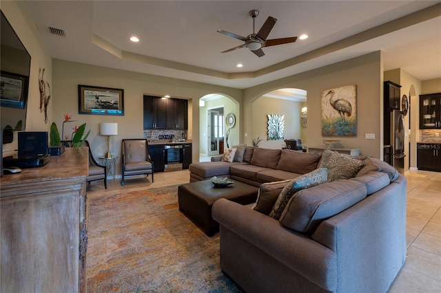 living area featuring a tray ceiling, light tile patterned flooring, arched walkways, and recessed lighting