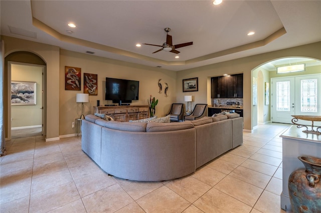 living room with recessed lighting, arched walkways, a raised ceiling, and light tile patterned flooring