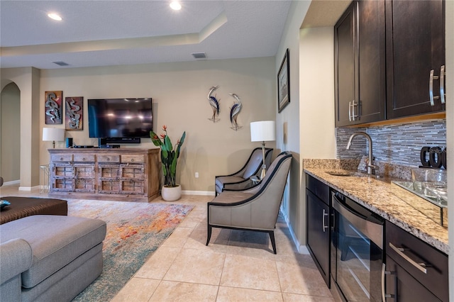 living area featuring arched walkways, light tile patterned floors, wine cooler, baseboards, and a raised ceiling