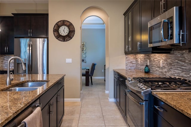 kitchen with light tile patterned floors, stone countertops, a sink, appliances with stainless steel finishes, and backsplash