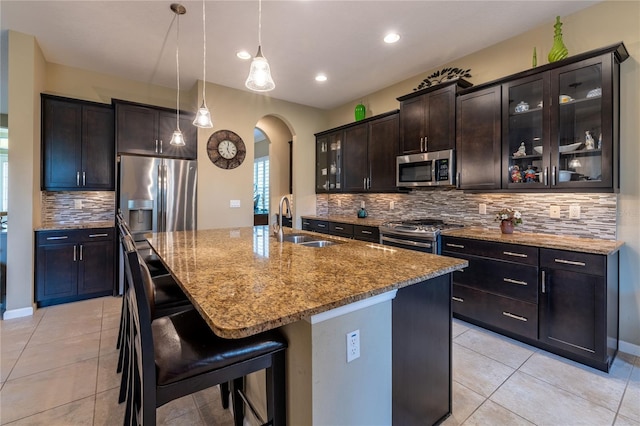 kitchen featuring light stone counters, arched walkways, light tile patterned floors, appliances with stainless steel finishes, and a sink