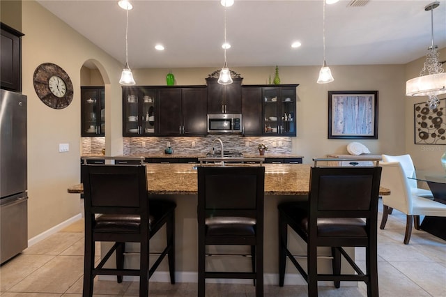 kitchen with arched walkways, stainless steel appliances, light stone counters, and backsplash